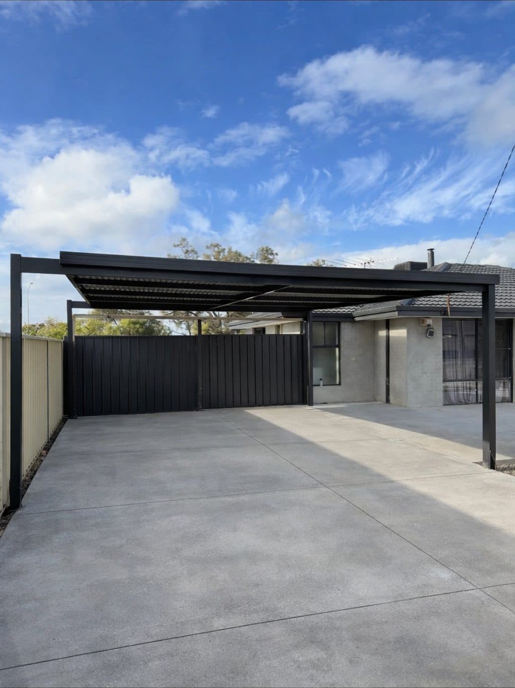 Modern flat roof carport with a dark steel frame over a concrete driveway at a Perth home