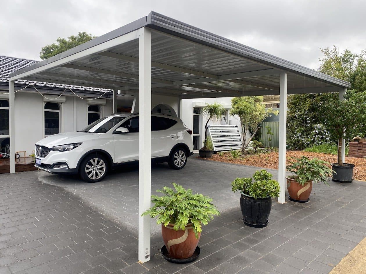 Flat roof steel carport over a paved driveway sheltering a car at a Perth home