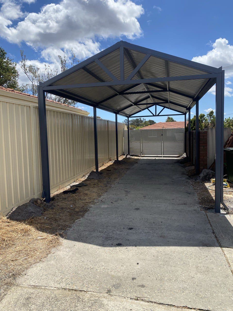 Gable carport with exposed steel trusses over a concrete driveway between Colorbond fences in Perth, WA